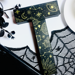 Load image into Gallery viewer, Decorative letter &#39;T&#39; with celestial designs on a white surface with black lace and flowers.
