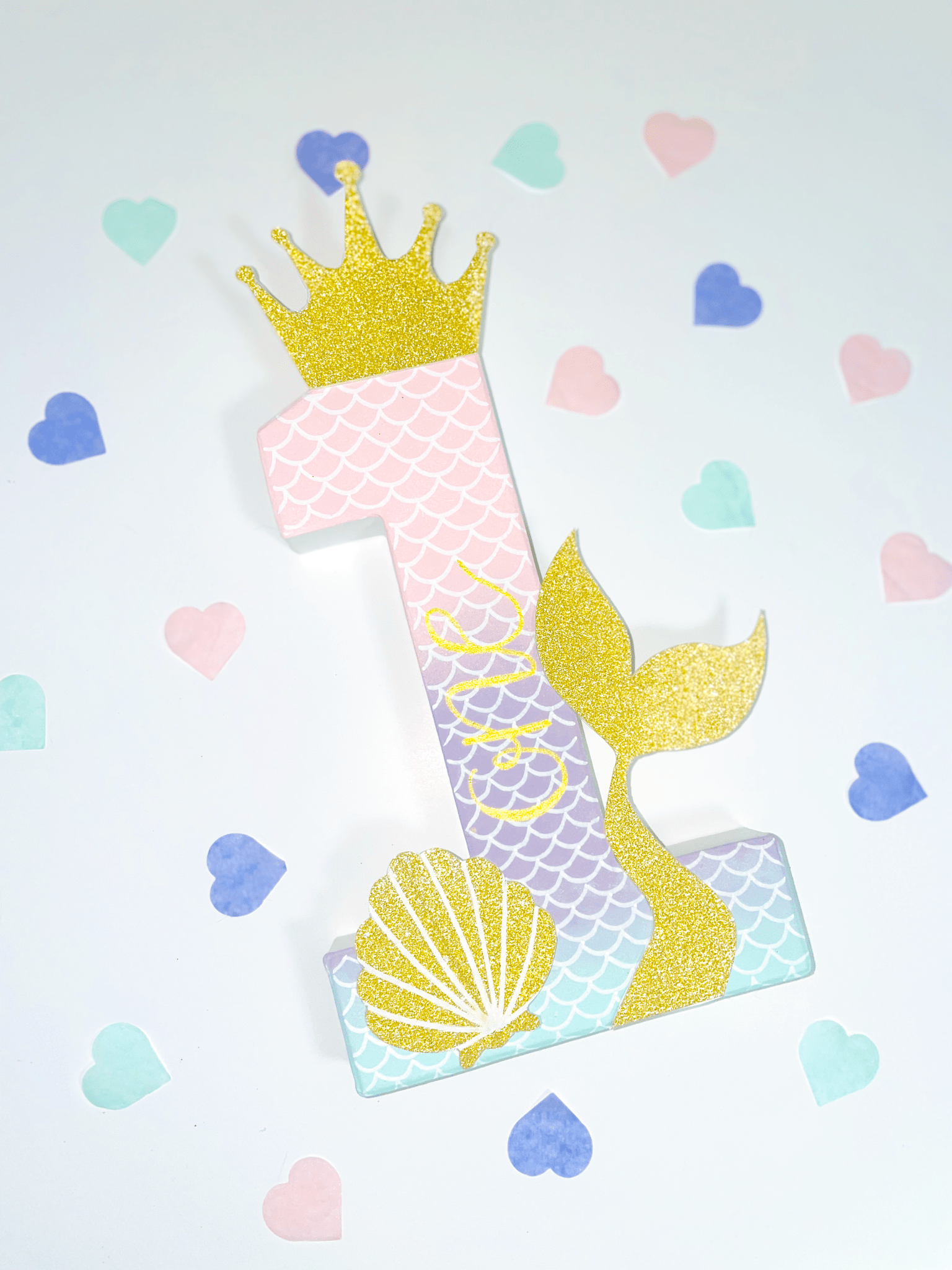Mermaid themed number '1' with a gold glitter crown, tail and shell on a white background with pastel confetti hearts scattered.