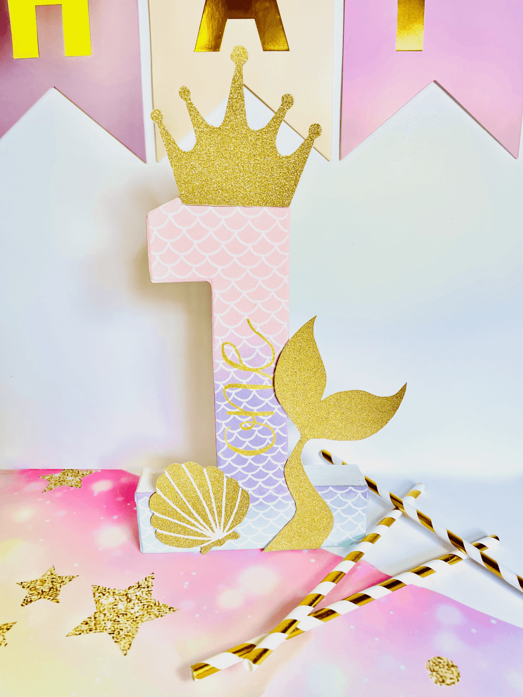 Ombre mermaid themed number '1' with a gold glitter crown, mermaid tail, and shell on a colourful background.